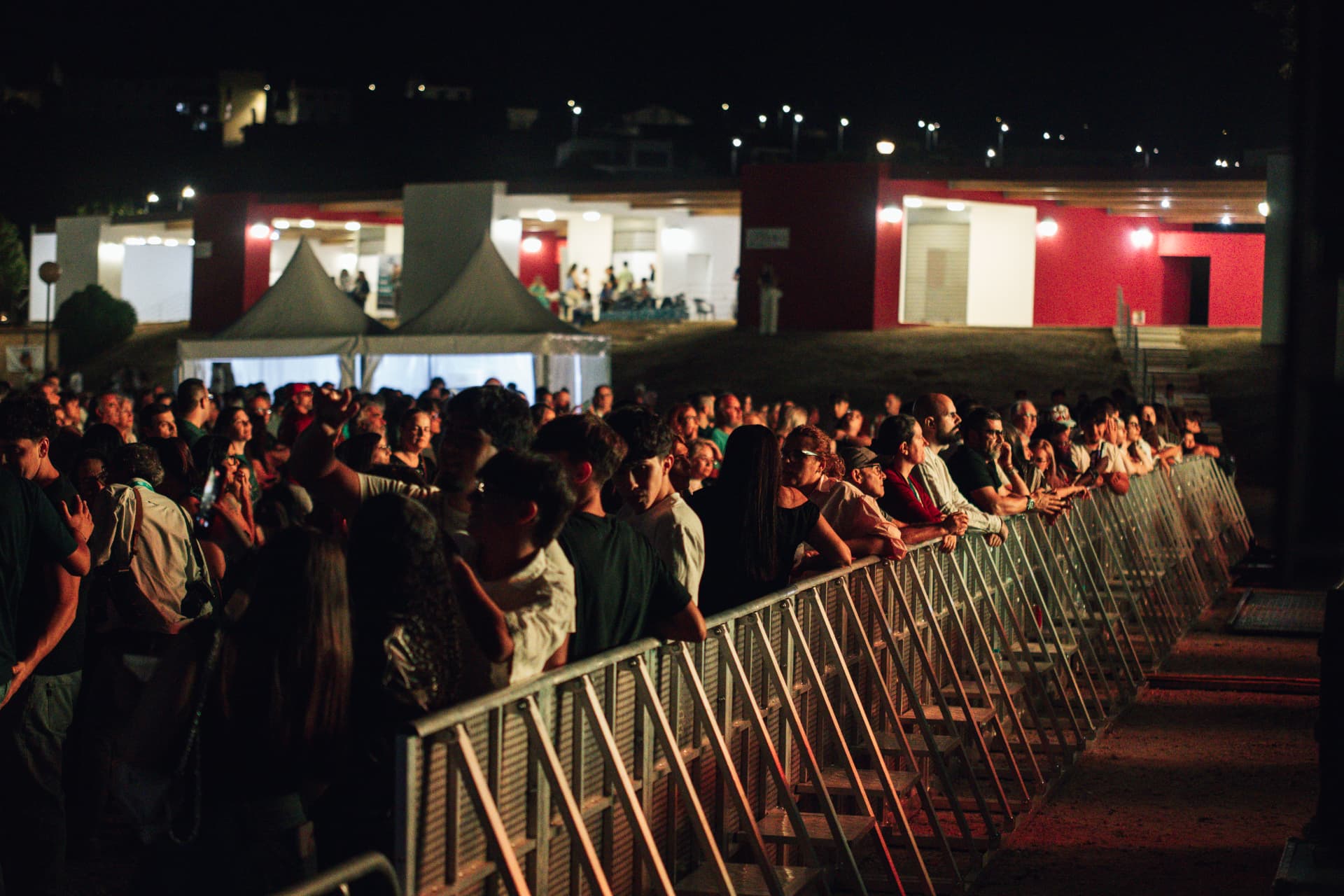 Público junto às grades com os pavilhões iluminados ao fundo