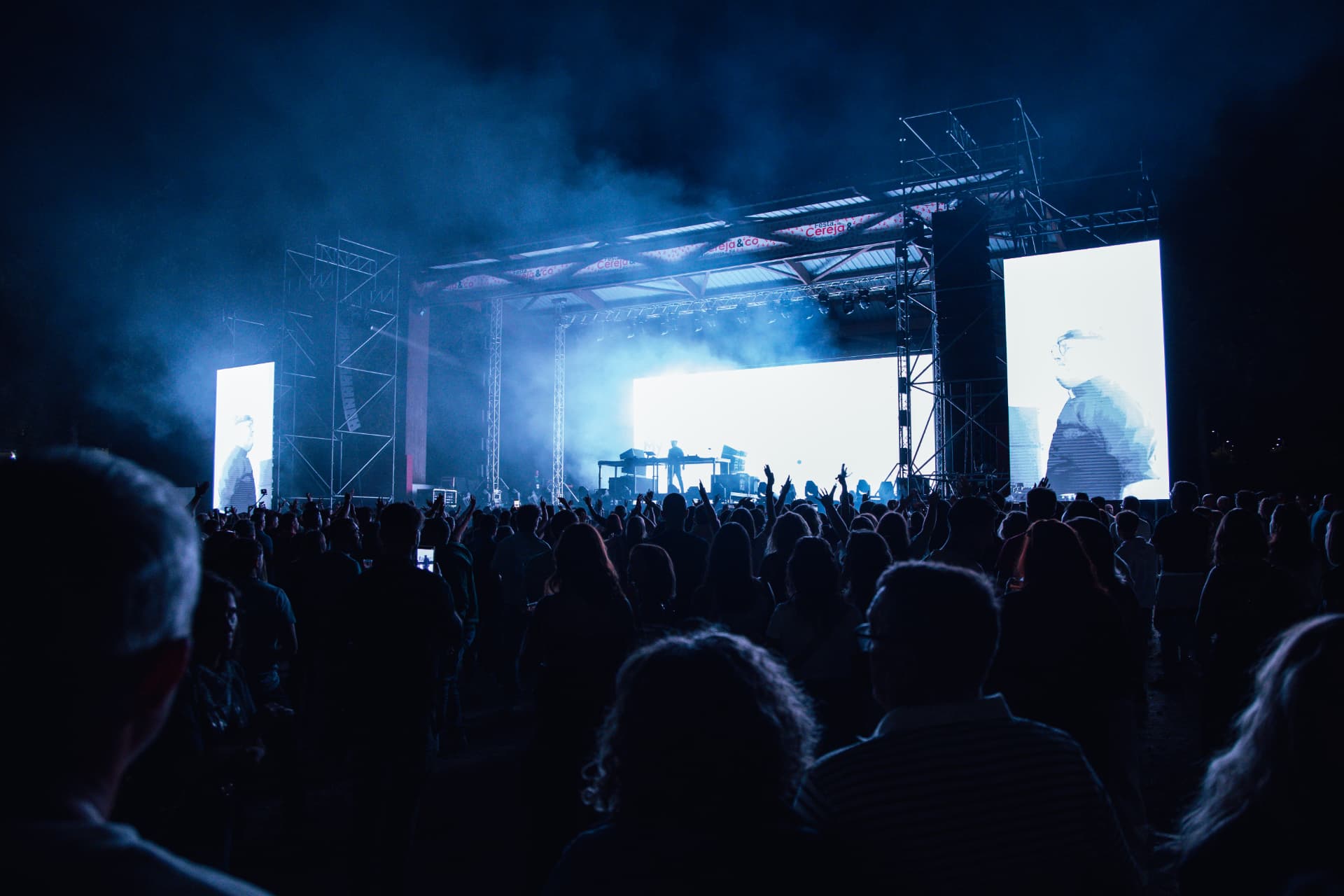 Palco iluminado de azul com fumo e o público em primeiro plano
