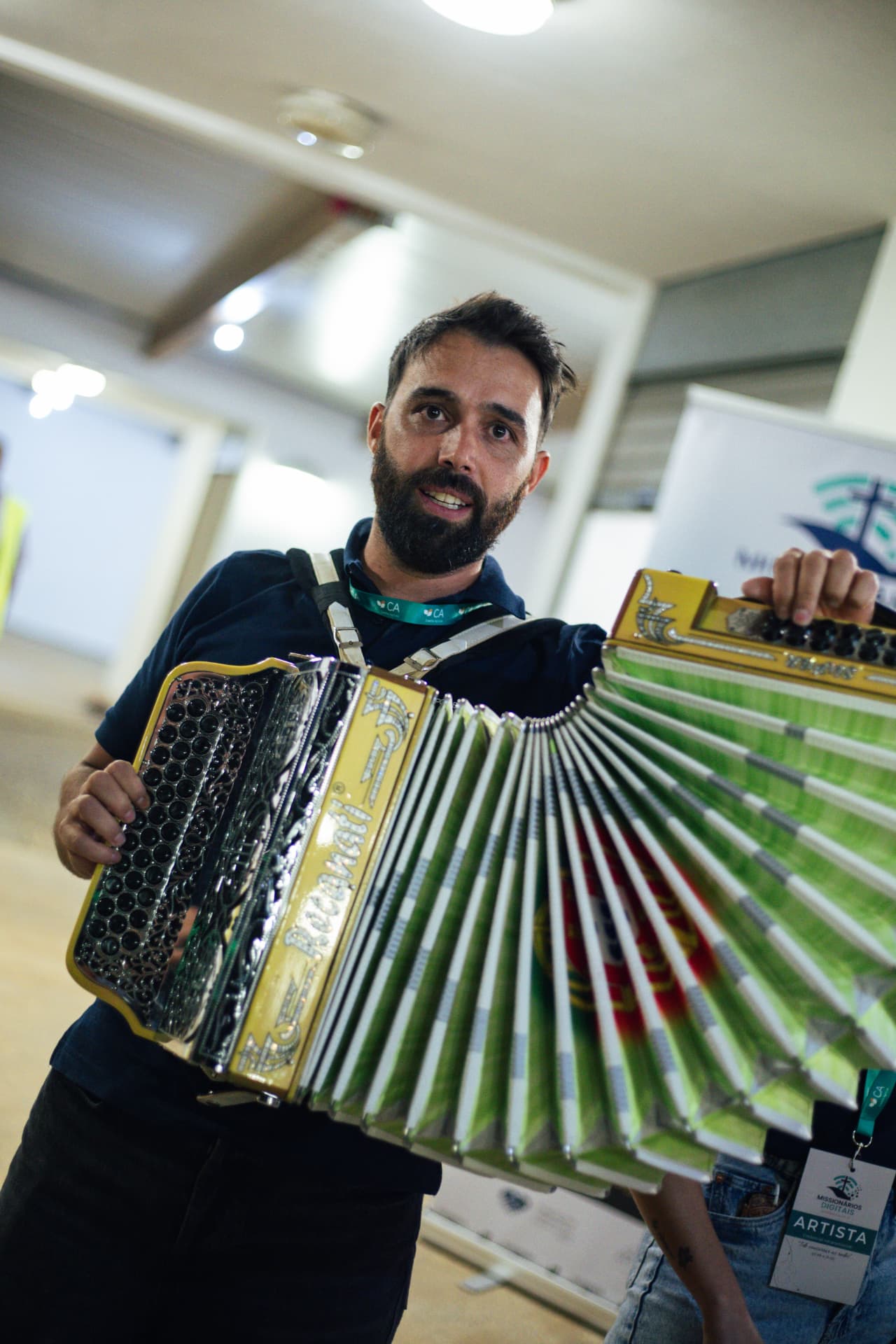 Músico mostra o acordeão amarelo e verde no corredor envidraçado