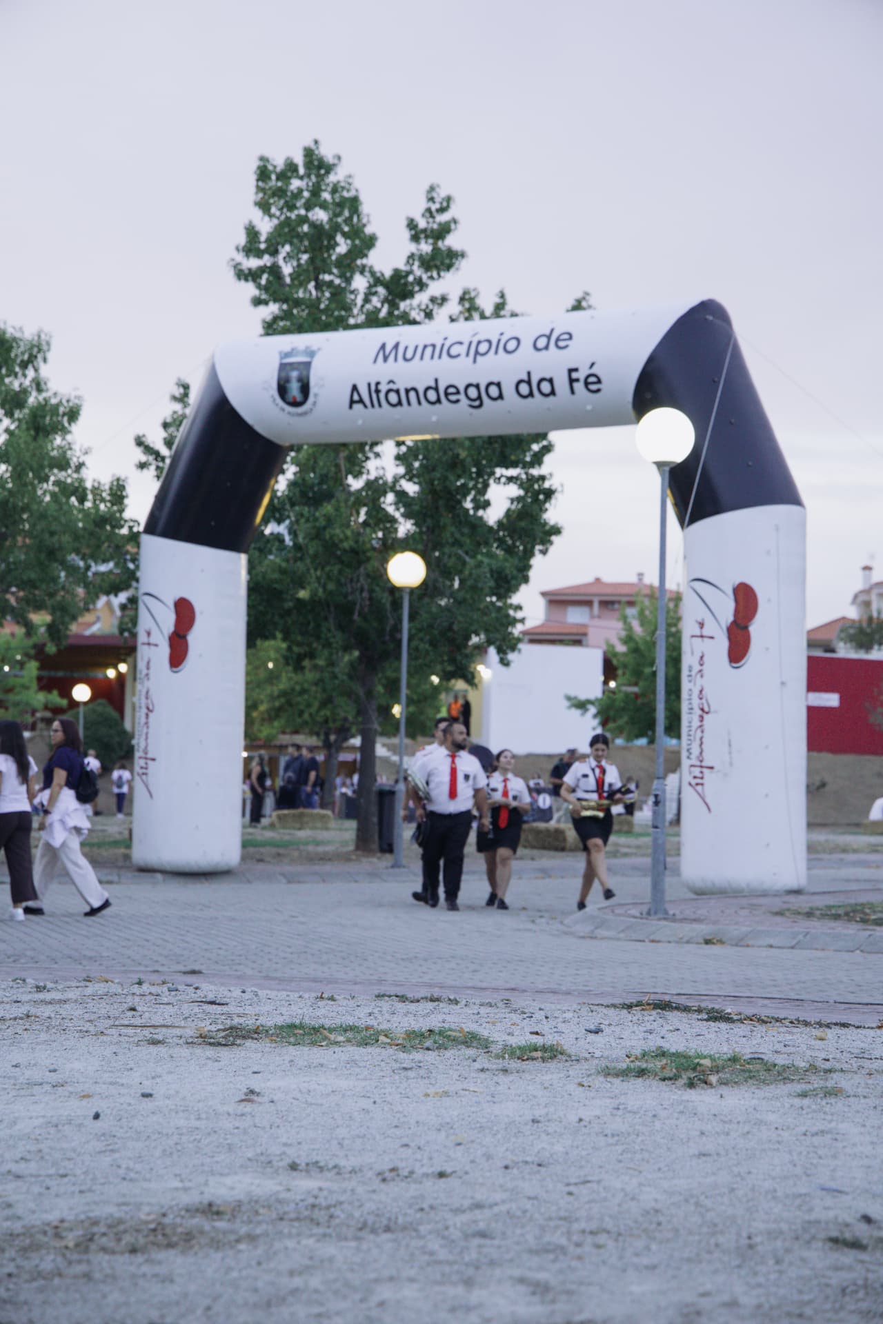 Participantes com gravatas vermelhas e um saxofone passam sob o arco inflável de entrada