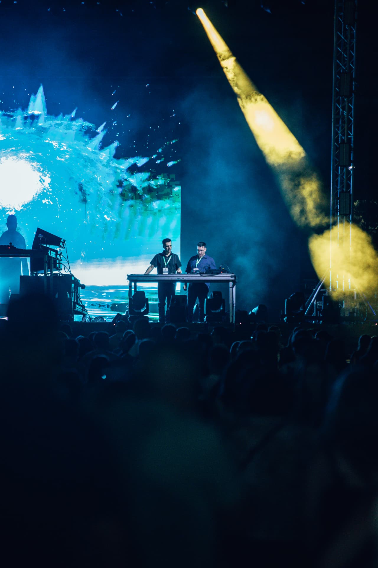 DJs em palco com ecrã azul e feixe de luz amarelo