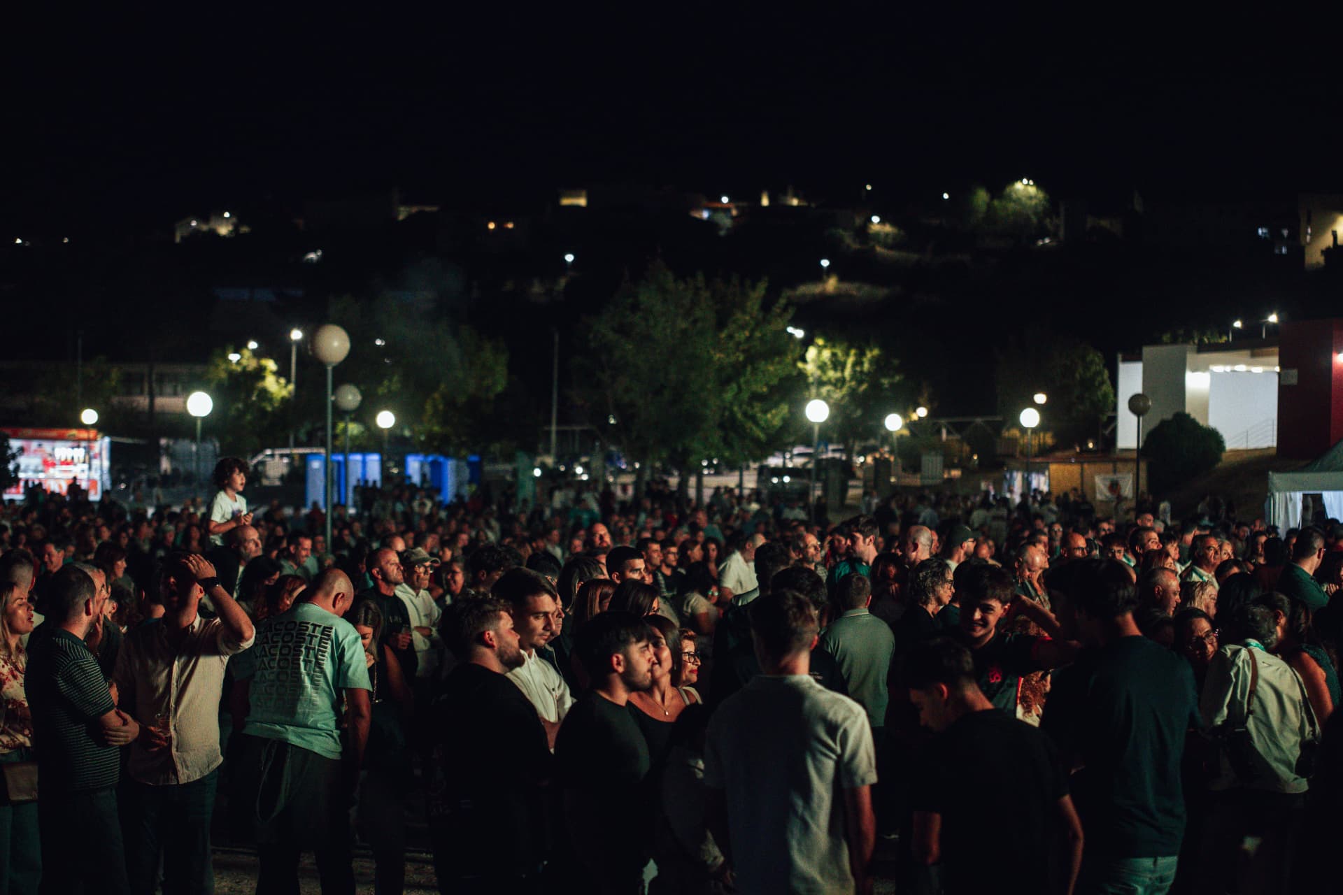 Multidão no recinto com a vila iluminada na encosta