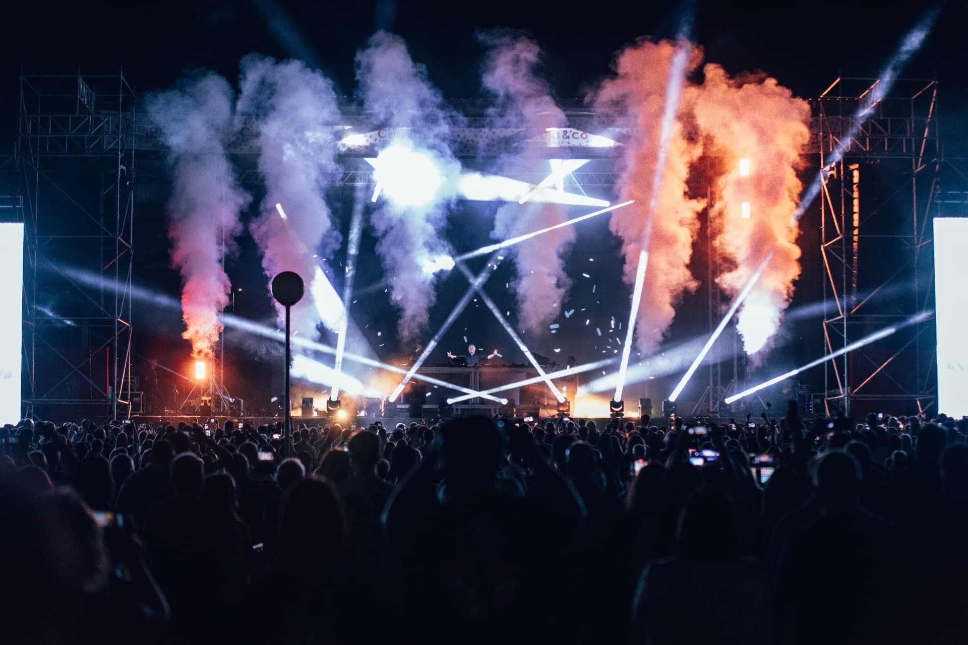 Palco em apoteose com fumo laranja e feixes cruzados