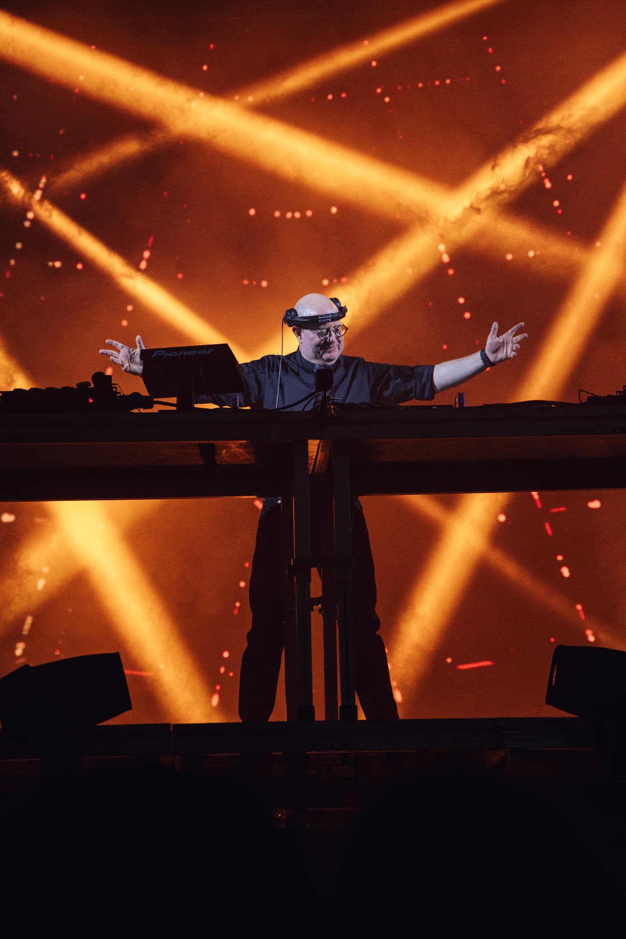 DJ com os braços estendidos sob feixes de luz dourada