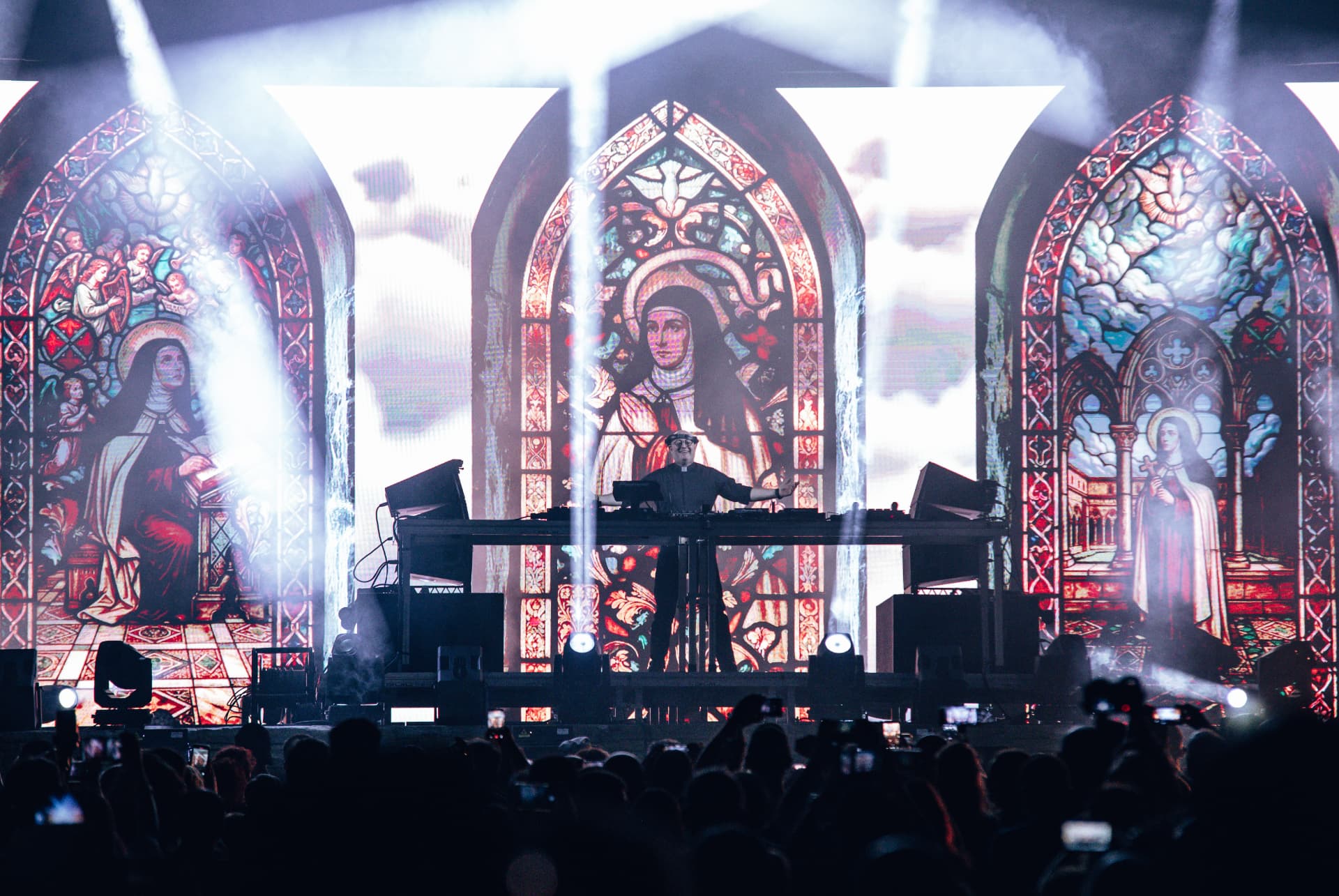 Padre Guilherme de braços abertos entre vitrais e feixes de luz