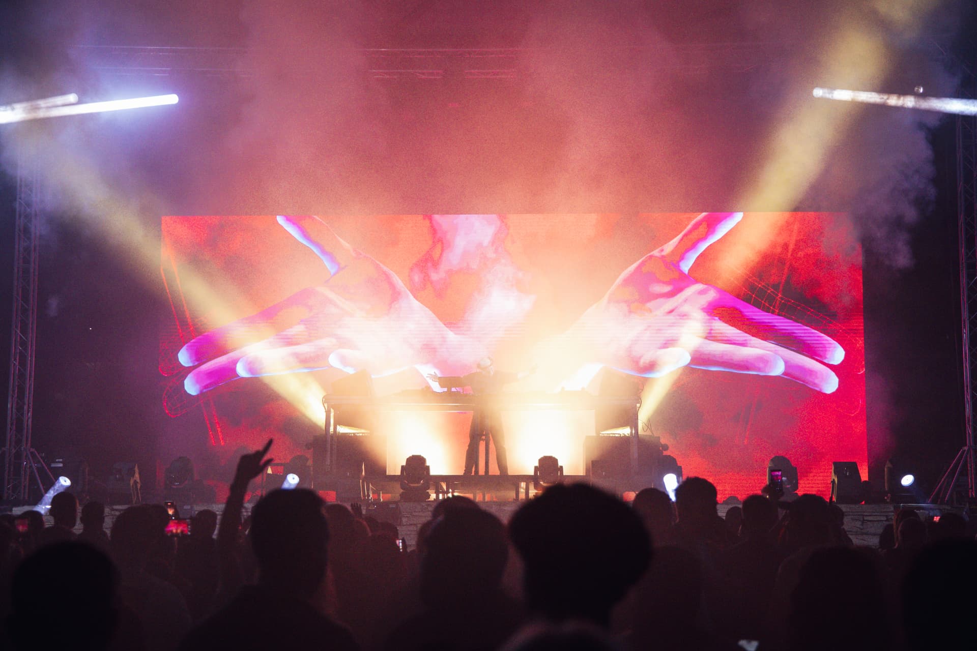DJ em palco diante de um grande ecrã com mãos projetadas em tons de fogo