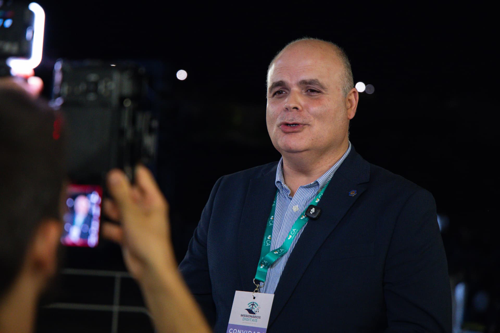Convidado com crachá de convidado é entrevistado diante das câmaras