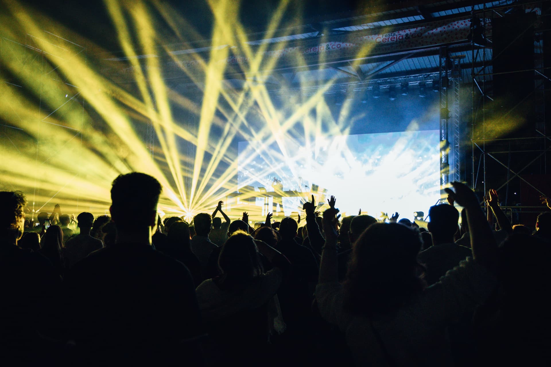 Multidão diante do palco iluminado por feixes amarelos