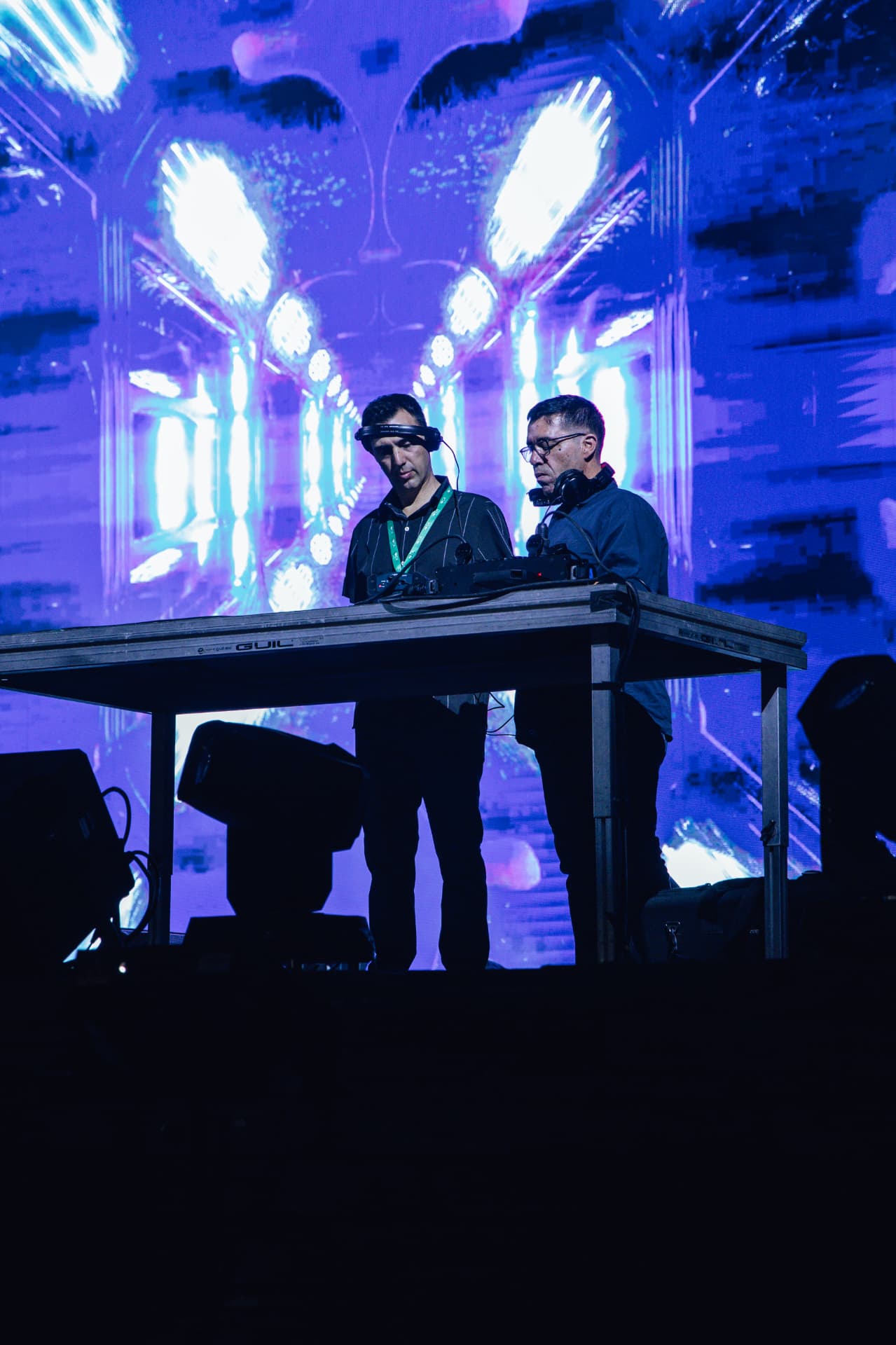 Dupla de DJs à mesa de mistura diante de ecrã violeta