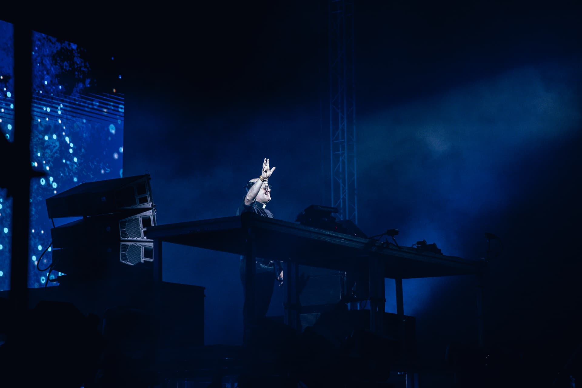 DJ com a mão levantada atrás da mesa de mistura