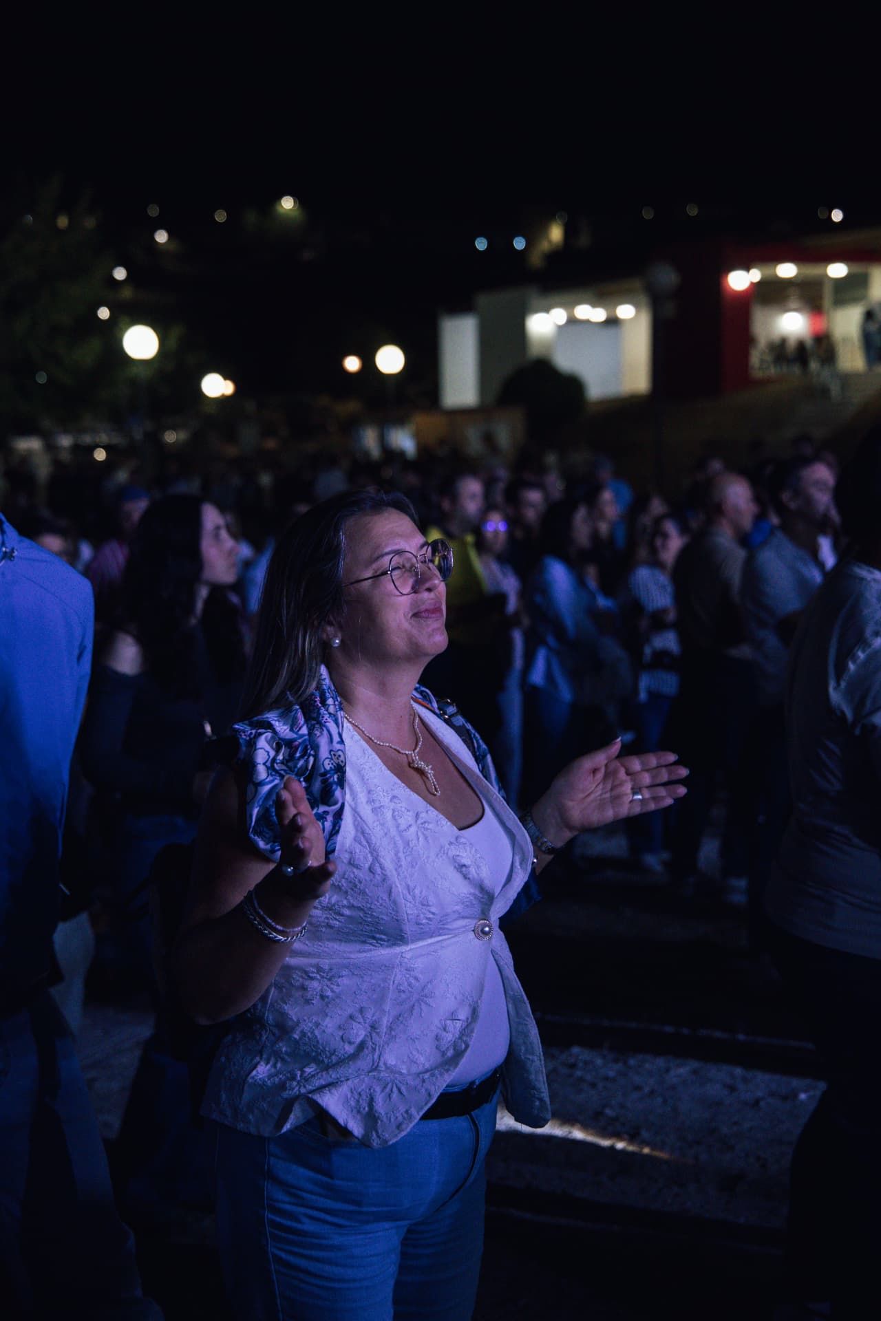Participante de olhos fechados em oração no meio da multidão, à noite